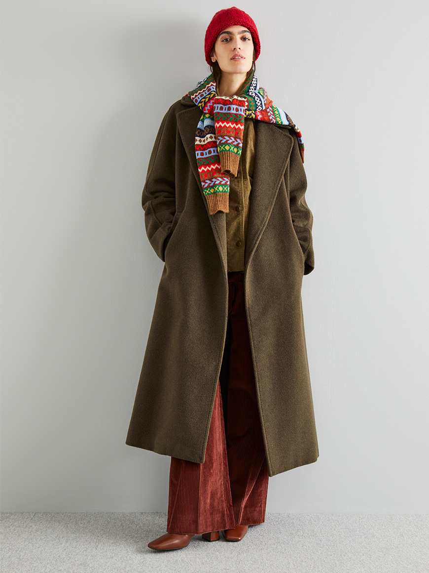 Modella indossa cappotto verde e pantaloni bordeaux.